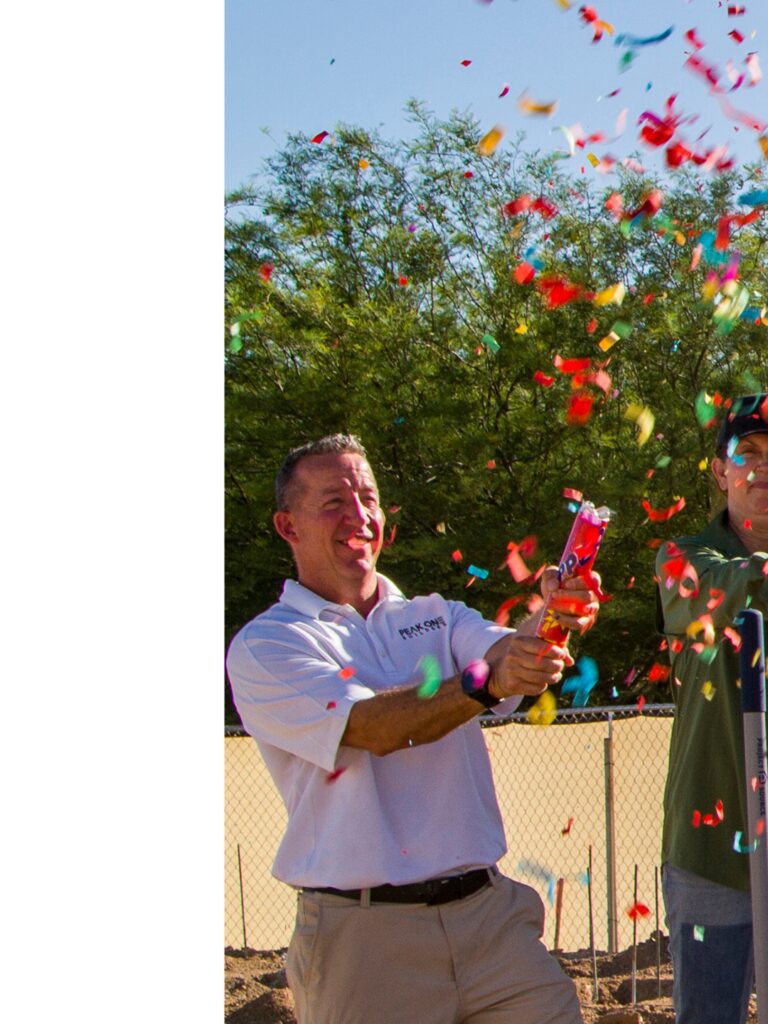 A group of people from Peak One Builders celebrating a groundbreaking with confetti flying in the air